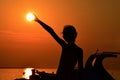 Silhouette of small girl holding sun during sunset above marina, part of motor boat visible on right side Royalty Free Stock Photo