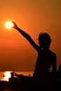 Silhouette of small girl holding sun during sunset above marina, part of motor boat visible on right side Royalty Free Stock Photo