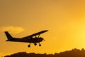 Silhouette of small propeller plane landing or taking off on the runway backlit under a yellow sun with the mountain below a Royalty Free Stock Photo