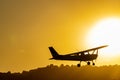 Silhouette of a small propeller plane landing or taking off on the runway backlit under a yellow sun at sunset Royalty Free Stock Photo