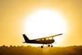 Silhouette of a small propeller plane landing or taking off on the runway backlit under a yellow sun at sunset Royalty Free Stock Photo