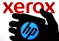 The silhouette of smartphone with HP logo hold in a hand and XEROX logo on the blurred background. Concept for takeover bid. Real Royalty Free Stock Photo