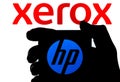 The silhouette of smartphone with HP logo hold in a hand and XEROX logo on the blurred background. Concept for takeover bid. Real Royalty Free Stock Photo