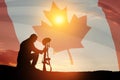 Silhouette of soldier kneeling with his head bowed on a background of sunset or sunrise and Canada flag.
