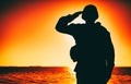 Silhouette of soldier salutes on sunset background