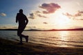 Silhouette of sport active man running and exercising on beach at vivid colorful sunset.