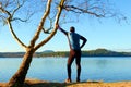 Silhouette of sport active man in running leggins and blue shirt at birch tree on beach. Calm water, island and sunny day Royalty Free Stock Photo