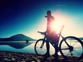 Silhouette of sportsman holding bicycle on lake beach, colorful sunset cloudy sky in background Royalty Free Stock Photo