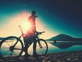 Silhouette of sportsman holding bicycle on lake beach, colorful sunset cloudy sky in background Royalty Free Stock Photo