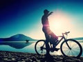 Silhouette of sportsman holding bicycle on lake beach, colorful sunset cloudy sky in background Royalty Free Stock Photo