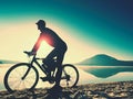 Silhouette of sportsman holding bicycle on lake beach, colorful sunset cloudy sky in background Royalty Free Stock Photo