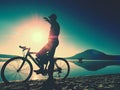 Silhouette of sportsman holding bicycle on lake beach, colorful sunset cloudy sky in background Royalty Free Stock Photo