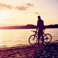 Silhouette of sportsman holding bicycle on lake bech, colorful sunset cloudy sky and reflection in wavy water level Royalty Free Stock Photo