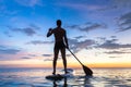 Silhouette of stand up paddle boarder paddling at sunset, sea