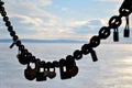 The silhouette of a steel chain with locks hanging on it against the backdrop of a frozen river and blue sky with white clouds. Royalty Free Stock Photo