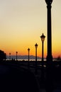 Silhouette of street lights during beautiful sunset. A couple walking by embankment Royalty Free Stock Photo