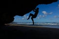 SILHOUETTE: Strong man climbs a big boulder near a stunning white sand beach.