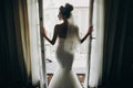 Silhouette of stylish bride opening window balcony in soft light in hotel room. Back of gorgeous sensual bride in white gown.