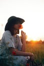 Silhouette of stylish girl in linen dress holding poppy flower in meadow in sun light with flowers in rustic straw basket. Boho Royalty Free Stock Photo