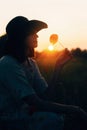 Silhouette of stylish girl in linen dress holding poppy flower in meadow in sun light with flowers in rustic straw basket. Boho Royalty Free Stock Photo