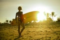 Silhouette with sun lens flare of young happy and attractive surfer girl carrying surf board posing on extreme backlight enjoying Royalty Free Stock Photo