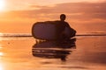 Silhouette of surf man sitting with a surfboard on the seashore beach at sunset time Royalty Free Stock Photo