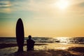 Silhouette of surf man sitting with a surfboard on the seashore