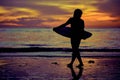 Silhouette of a surfer heading into the water during sunrise.