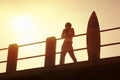 Silhouette of surfer on pier at sunrise with surfboard Royalty Free Stock Photo
