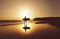 Silhouette of surfer walking along beach at sunrise