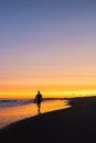 Silhouette of a surfer walking with motion blur, as a vibrant colorful sunset lights up the sky above the beach. Long Beach NY