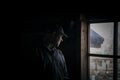 Silhouette of a suspicious strange man looking out the window in a scary dark attic of an old abandoned house in the darkness, Royalty Free Stock Photo