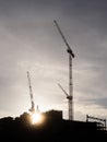 Silhouette of tall construction cranes at sunset. Dark moody sky. Construction industry. Building new commercial office of