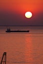 Silhouette of tank ship moored at anchor against red sunset sky