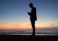 Silhouette of a teenage boy standing on a beach at sunset