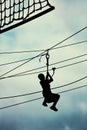 Silhouette of a teenage boy ziplining on zipline against cloudy sky background