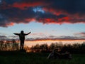 Silhouette of a teenager girl with her small yorkshire terrier in a field against beautiful sunset sky. Dog is in foreground, the