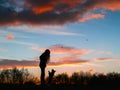 Silhouette of a teenager girl with her small yorkshire terrier in a field against beautiful sunset sky. Dog is on its rear feet.