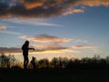 Silhouette of a teenager girl with her small yorkshire terrier in a field against beautiful sunset sky. Girl has a toy in her hand