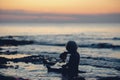 Silhouette of a toddler boy sitting in shallow water of an ocean