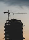 Silhouette of tower cranes in operation at construction site with during sunset. Real estate development concept.