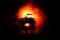 Silhouette of tractor at night with dark foggy background. Toned. Burning vehicle.