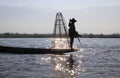 Silhouette of traditional fisherman balancing on his boat and rowing with his feed on Inle Lake, Myanmar