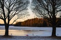 Silhouette of trees side by side with the sunset shining towards the forest`s trees and reflecting into the lake`s waters Royalty Free Stock Photo