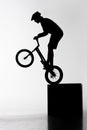 silhouette of trial biker performing stunt while balancing on cube