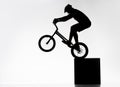silhouette of trial cyclist performing back wheel stand while balancing on cube