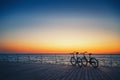 Silhouette of two bicycles at the beach at sunrise sky at wooden deck summer time, ride along seashore summer beach at yellow blue