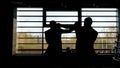 Silhouette of two boxers having a fight in a dark room in front of a window with sunlight. Stock footage. Side view of