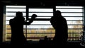 Silhouette of two boxers having a fight in a dark room in front of a window with sunlight. Stock footage. Side view of