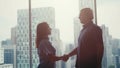 Silhouette of two businessmen talking and shaking hands standing by the window urban city view in the background at Royalty Free Stock Photo